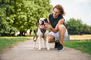 sporty young man kneeling next to leashed mixed breed dog at the park