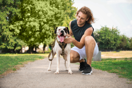 sporty young man kneeling next to leashed mixed breed dog at the park